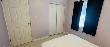 A bedroom with a bed, two doors, and a window with curtains.