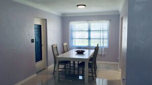 Une salle à manger avec une table et des chaises, une fenêtre avec des stores et une porte.