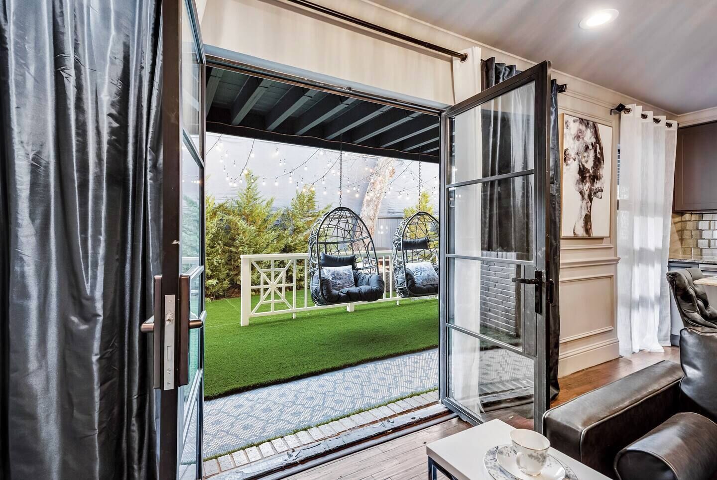Un interno moderno con una porta in vetro che dà su una zona esterna con due poltrone a sacco sospese e una struttura a reticolo bianca.