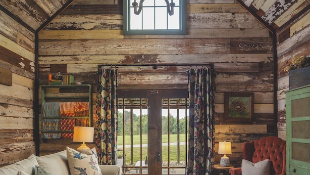 Interno di una baita rustica con soffitto in legno, una grande finestra, un divano, una poltrona e un tavolino.