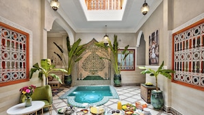 Un interior tradicional marroquí con una zona de estar central, decoración ornamentada y una mesa para comer.