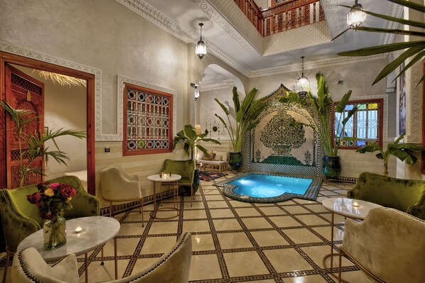 Une chambre luxueuse avec un sol carrelé, une petite piscine et des meubles richement décorés.