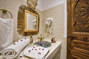 Une salle de bain équipée d’un lavabo, d’un miroir, d’un sèche-cheveux, d’une serviette et d’objets décoratifs.