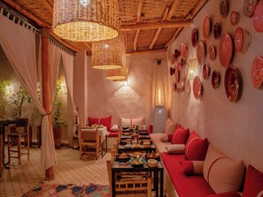 A cozy dining area with a long table, red cushions, and a variety of dishes. - Riad Arabkech (Marrakech)