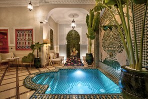 Une piscine intérieure luxueuse, dont le sol est recouvert de carreaux disposés en motif à damier, et qui est entourée d’une décoration et de meubles élégants.