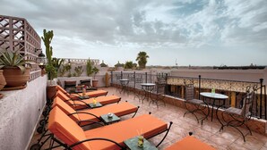 Una terraza en la azotea con asientos anaranjados, vistas al mar y una planta de cactus decorativa.