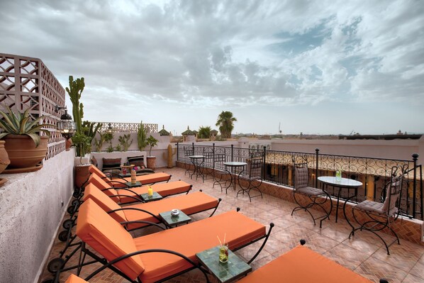A rooftop terrace with orange seating, a view of the sea, and a decorative cactus plant. - Riad Arabkech (Marrakech)