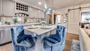Una cucina moderna con piani di lavoro in marmo, elettrodomestici in acciaio inossidabile e un'isola centrale con sedie in velluto blu.