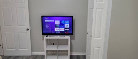 A television on a white stand with a menu interface, set against a grey wall with white doors.