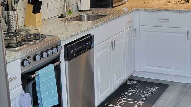Una cocina moderna con armarios blancos, lavavajillas, estufa y microondas.