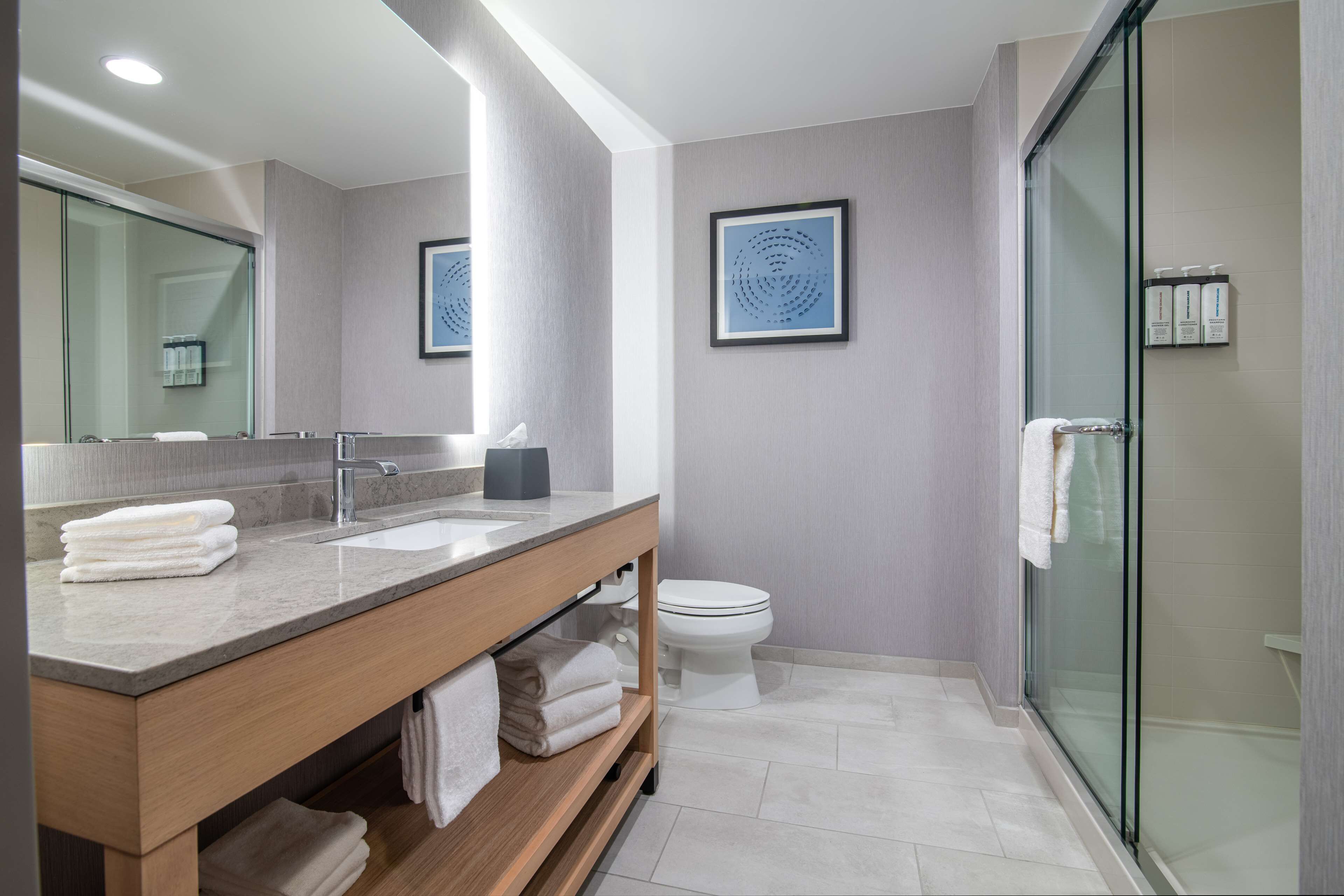 A modern bathroom with a wooden vanity, a glass shower enclosure, and a toilet.