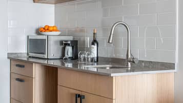 A modern kitchen with wooden cabinets, a built-in microwave, a coffee maker, and a wine bottle.