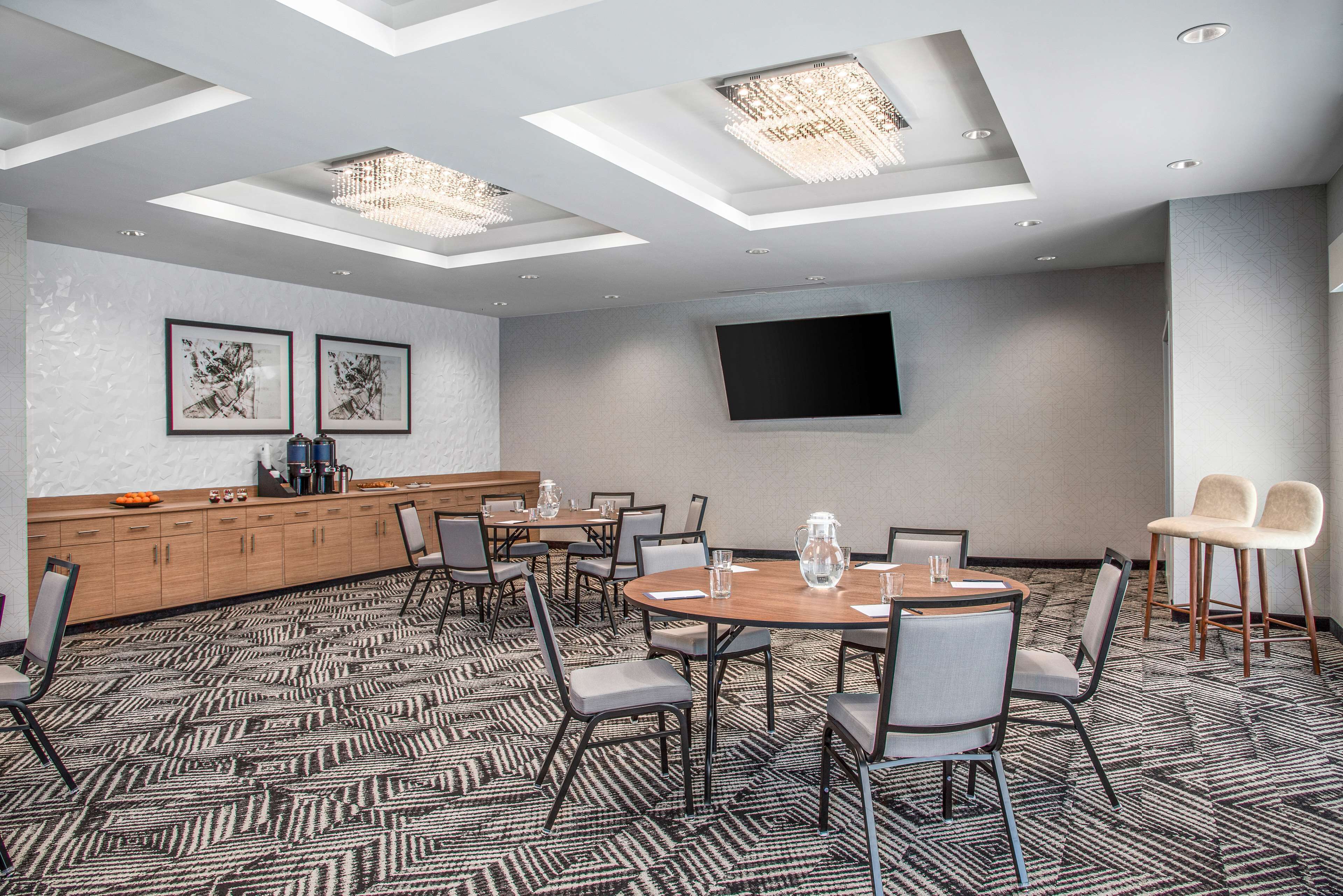 A conference room with a large table, chairs, a wooden cabinet, and a flat-screen TV on the wall.