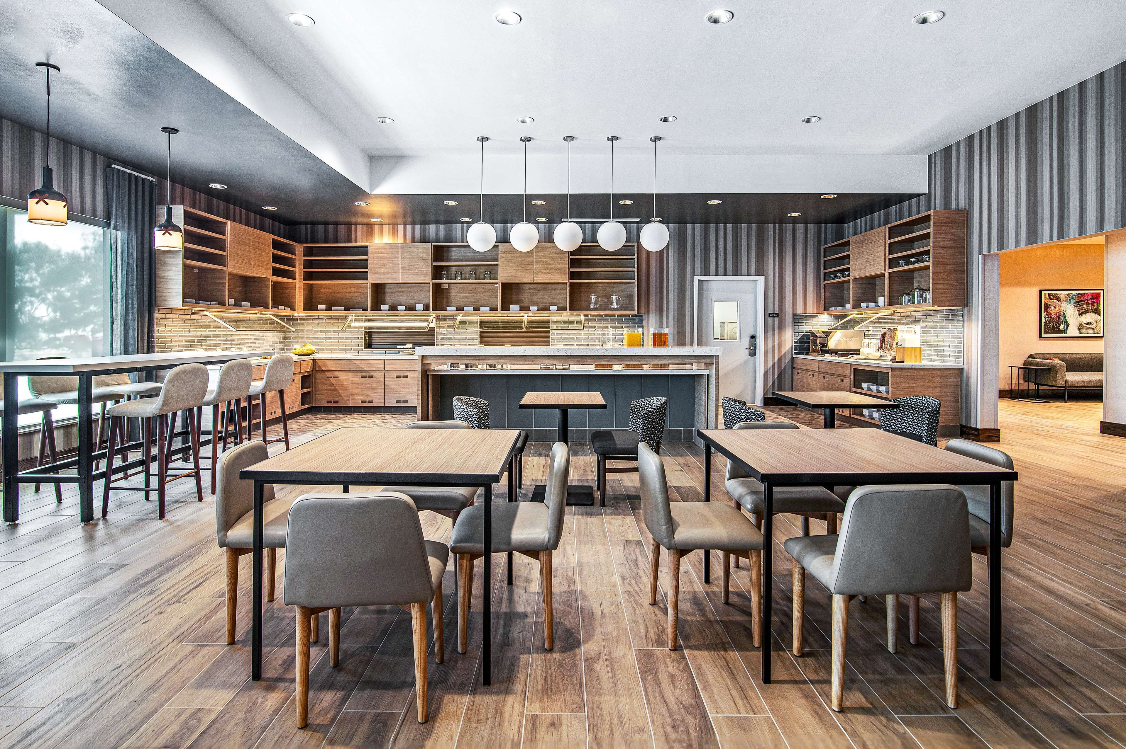 Un restaurant moderne avec des tables et des chaises en bois, un bar central et une vue sur l’extérieur.