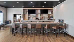 Eine moderne Bar mit einer langen Theke, Barhocker und Regalen voller Flaschen und Gläsern.