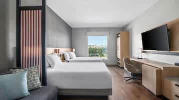 A modern hotel room with two beds, a desk, a TV, and a view of the outdoors.