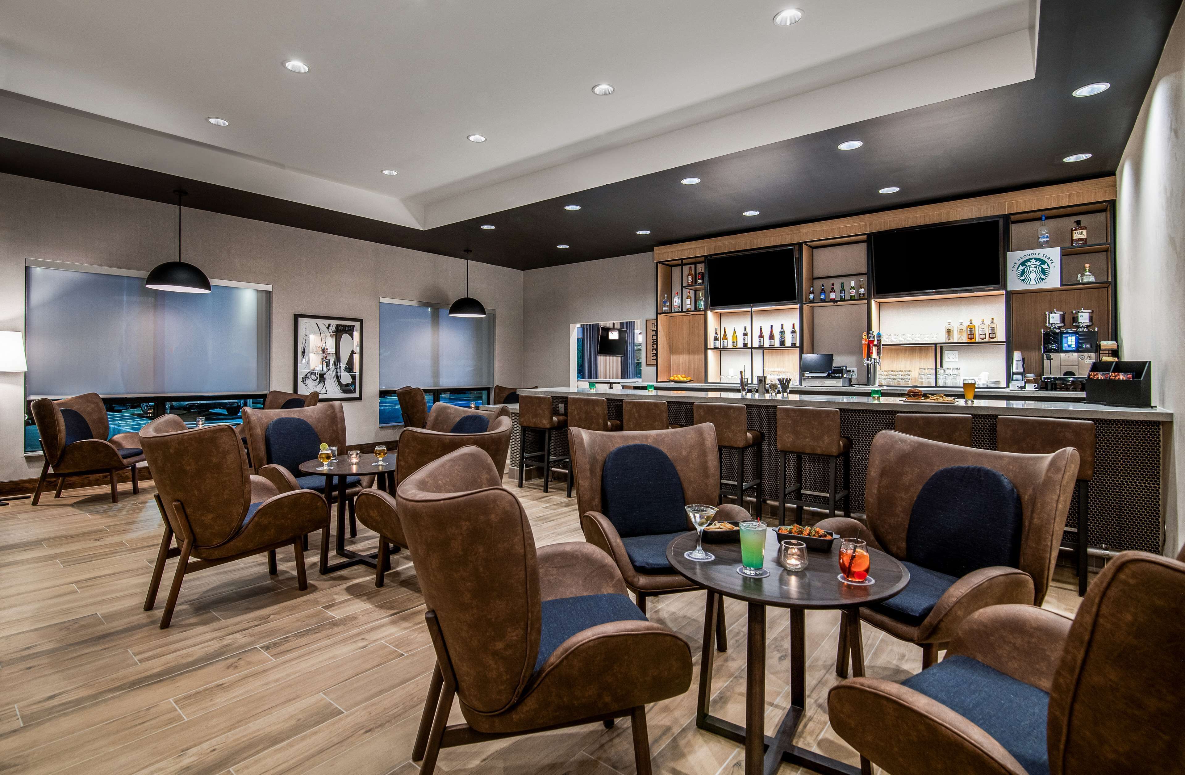 A modern bar area with seating and a bar counter, featuring wooden flooring and contemporary furniture.