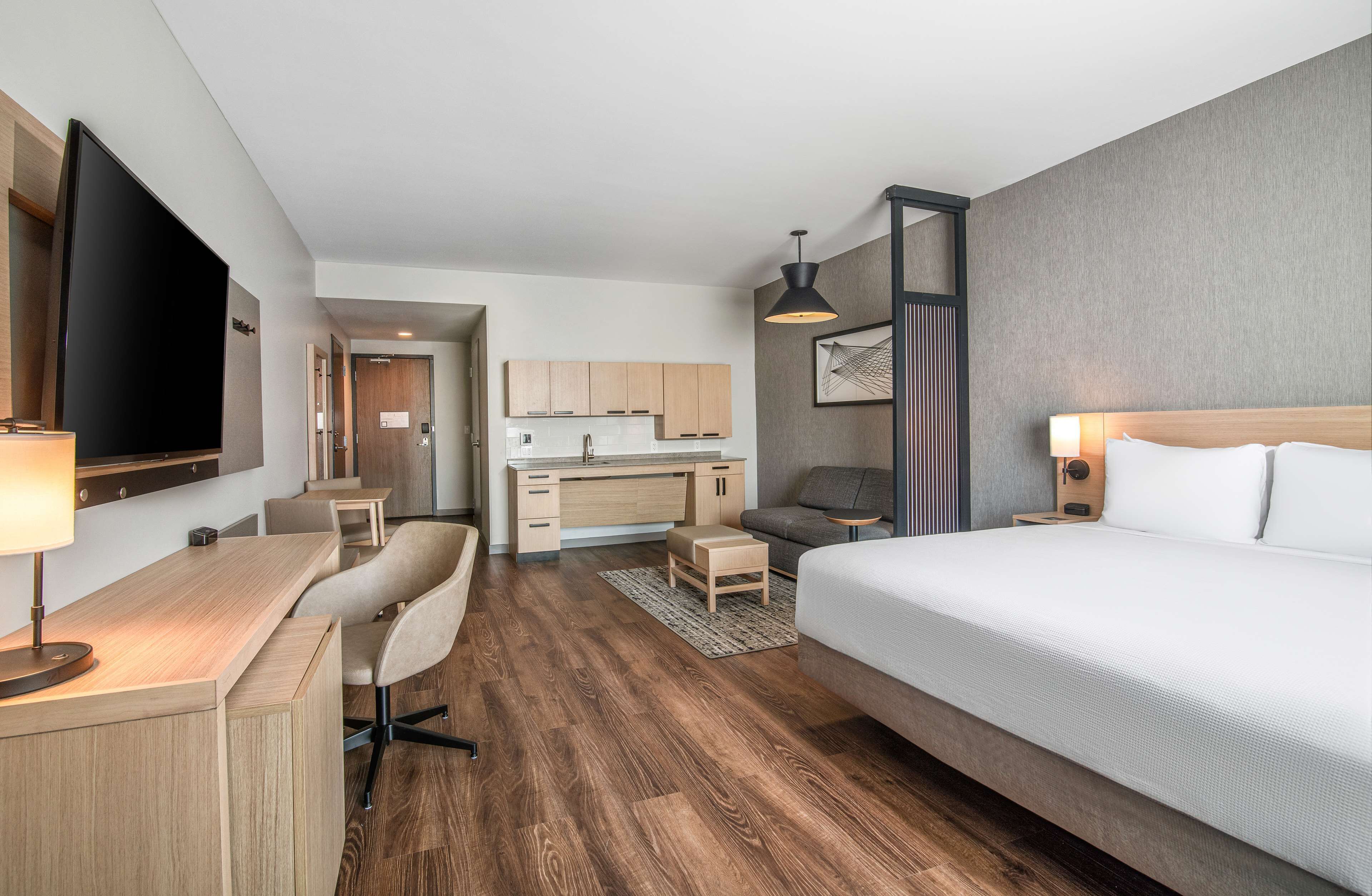 A hotel room with a bed, desk, chair, and kitchenette.