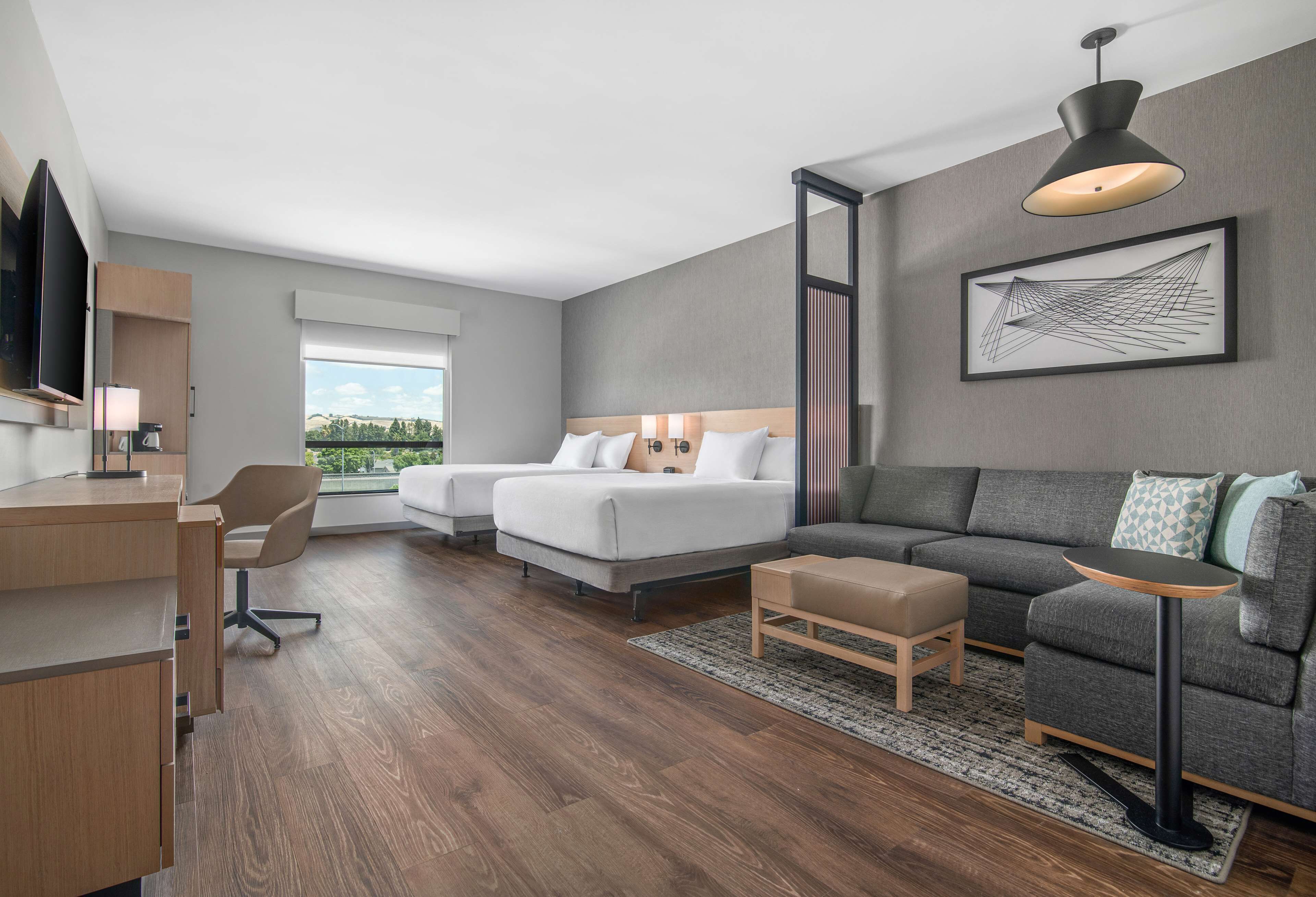 A modern hotel room with a large bed, a sofa, a desk, and a TV.