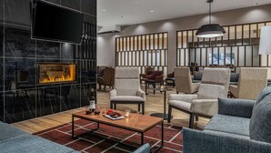 Ein moderner Lounge-Bereich mit Kamin, bequemen Sitzgelegenheiten und Blick auf die Stadt durch große Fenster.