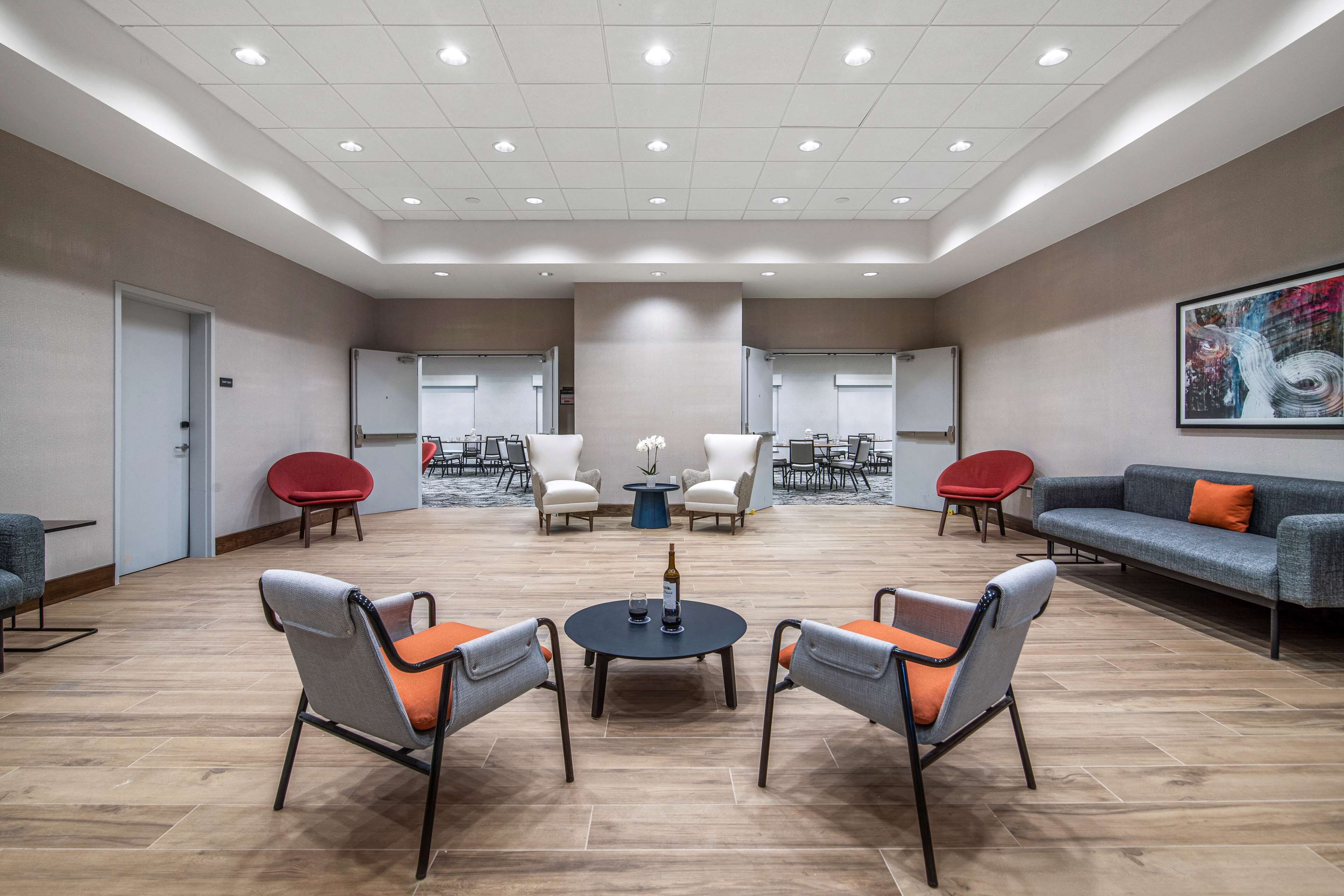 A spacious lounge area with a central round table, seating arrangements, and a large abstract painting on the wall.