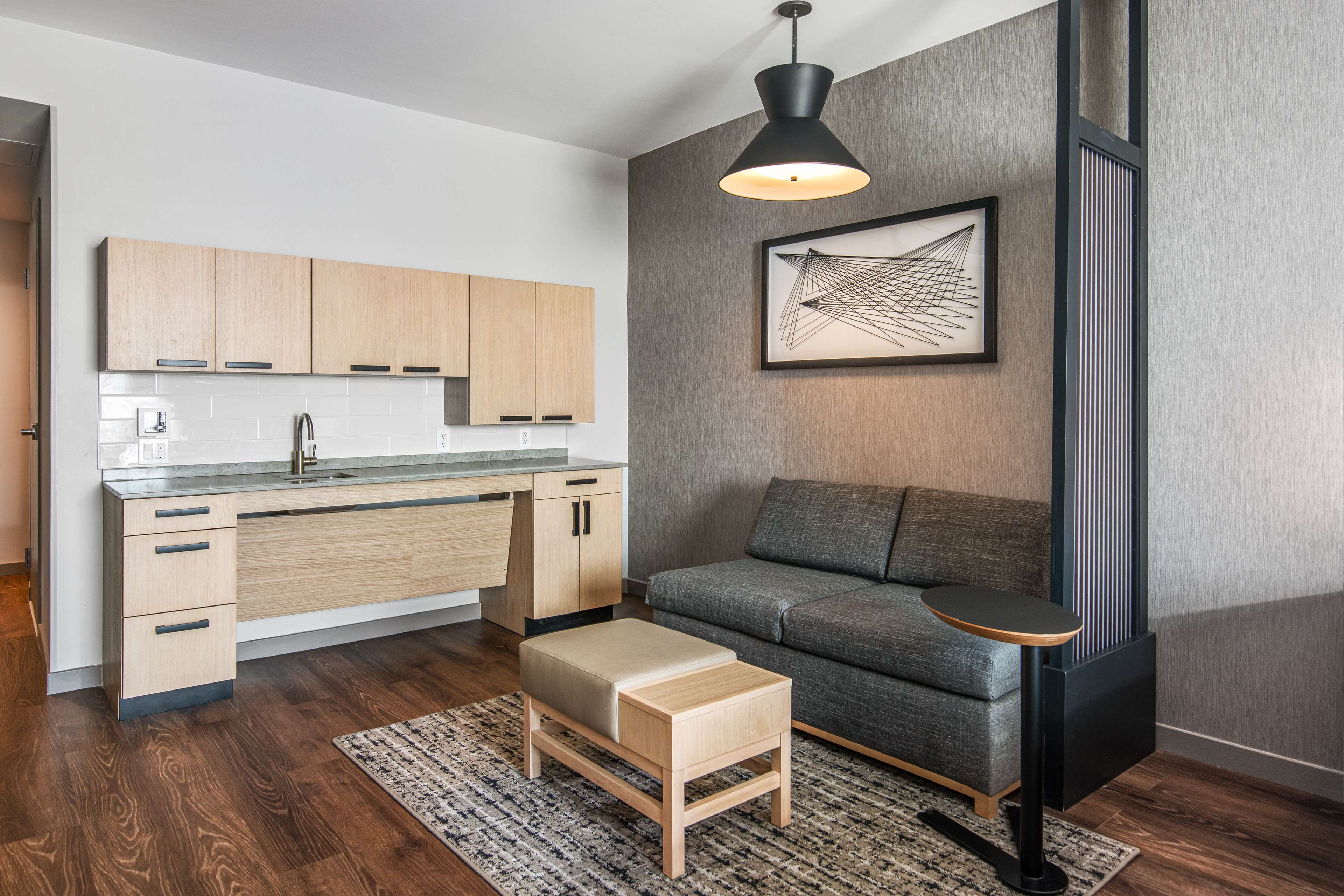 A modern kitchen with wooden cabinets, a built-in oven, and a dining area with a small table and bench.