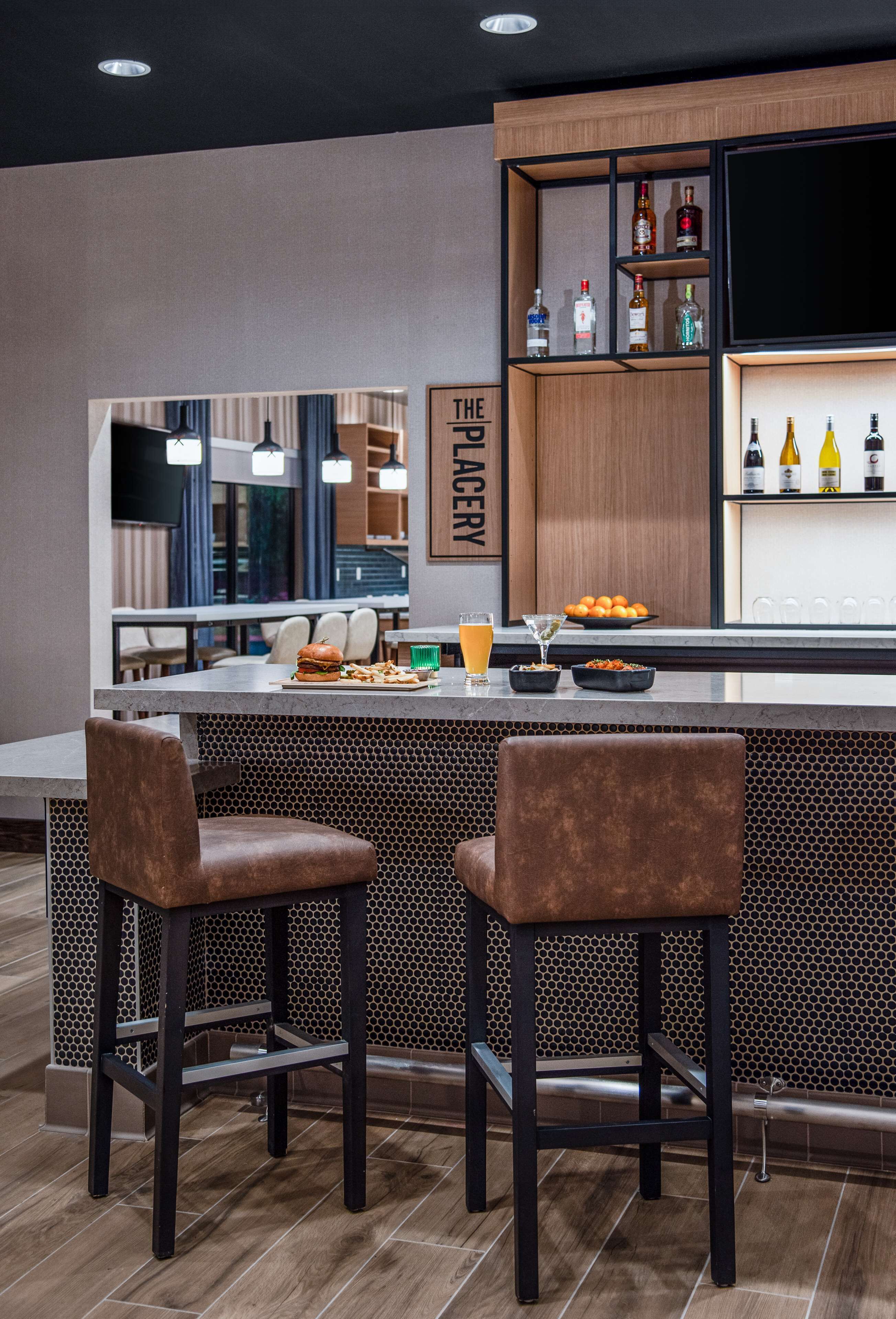 A modern bar area with a counter, stools, and a shelf with bottles.