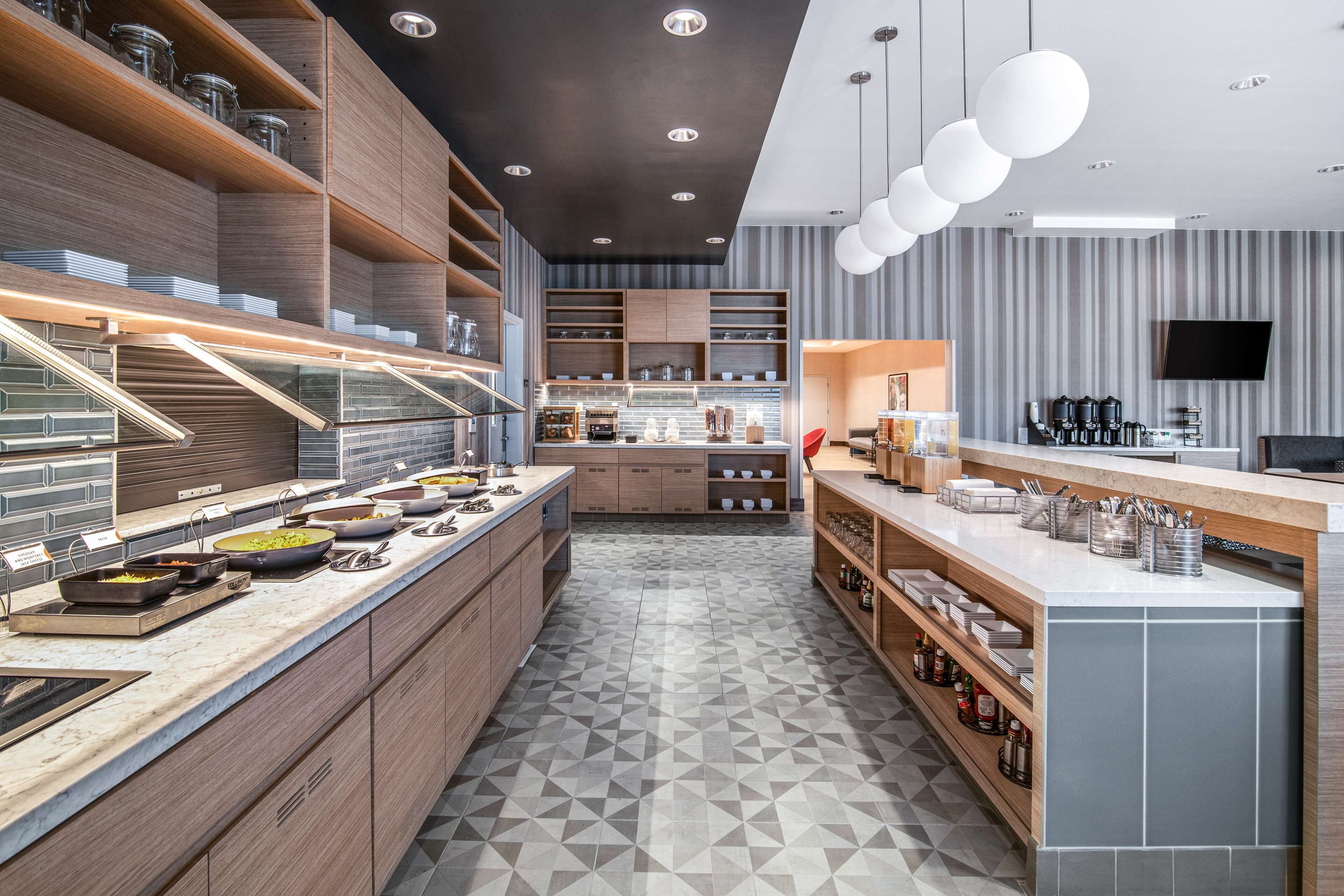 Une cuisine moderne dotée d’appareils électroménagers intégrés, de meubles de rangement en bois et d’un sol orné de motifs géométriques.