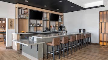 Un área de bar moderna con una barra larga, varias estanterías con botellas y taburetes de bar.