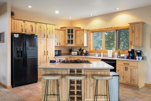 A kitchen with wooden cabinets, a black refrigerator, a stove, and a large island with stools. - Sleeps 16| Private Hot Tub, Game Room & Panoramic Views! (Grand Lake)