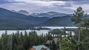 A cabin with a metal roof, surrounded by dense forest and mountains in the background.