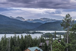 A cabin with a metal roof, surrounded by dense forest and mountains in the background.