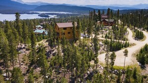A lodge surrounded by dense forest, with a clear view of a lake and mountains in the distance.
