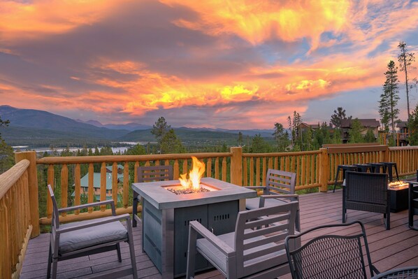 An outdoor deck with a fire feature, seating, and a view of mountains and a lake. - Sleeps 16| Private Hot Tub, Game Room & Panoramic Views! (Grand Lake)