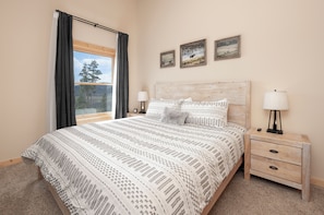 A bedroom with a large bed, two bedside tables with lamps, a wooden headboard, and three framed pictures on the wall.
