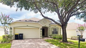 A single-story house with a garage, a brick driveway, and a large tree in front. - South facing pool home with hot tub and games room - gated community (Davenport)