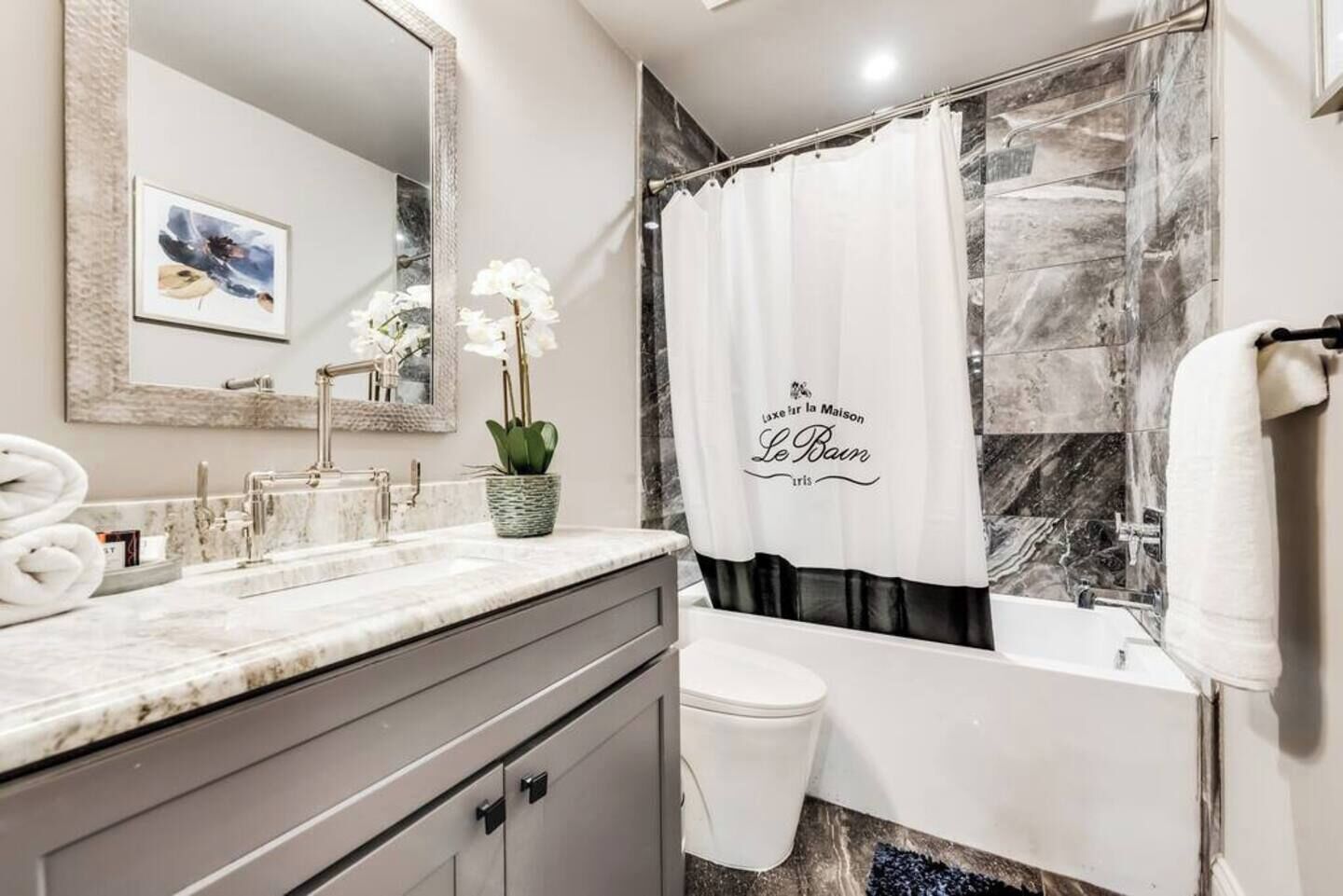 A bathroom with a marble sink, a white toilet, a bathtub, and a shower curtain with text.