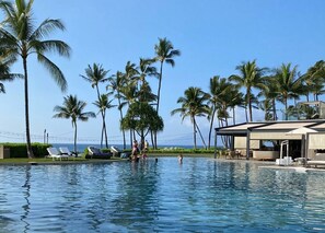 A pool area with palm trees, lounge chairs, and a view of the ocean.