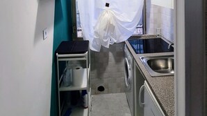 Een smalle keuken met een wasmachine, een spoelbak en een klein schap met schoonmaakmiddelen.
