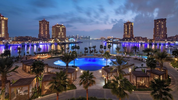 A resort with a large pool, palm trees, and city skyline views. - The St. Regis Marsa Arabia Island, The Pearl Qatar (Doha)