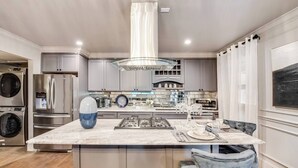 Une cuisine moderne dotée d’appareils électroménagers en acier inoxydable, d’un îlot en marbre et d’un luminaire suspendu.