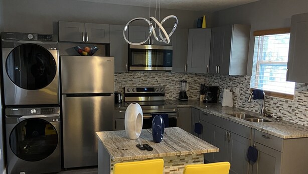 A modern kitchen with stainless steel appliances, a tiled backsplash, and a dining area with yellow chairs.