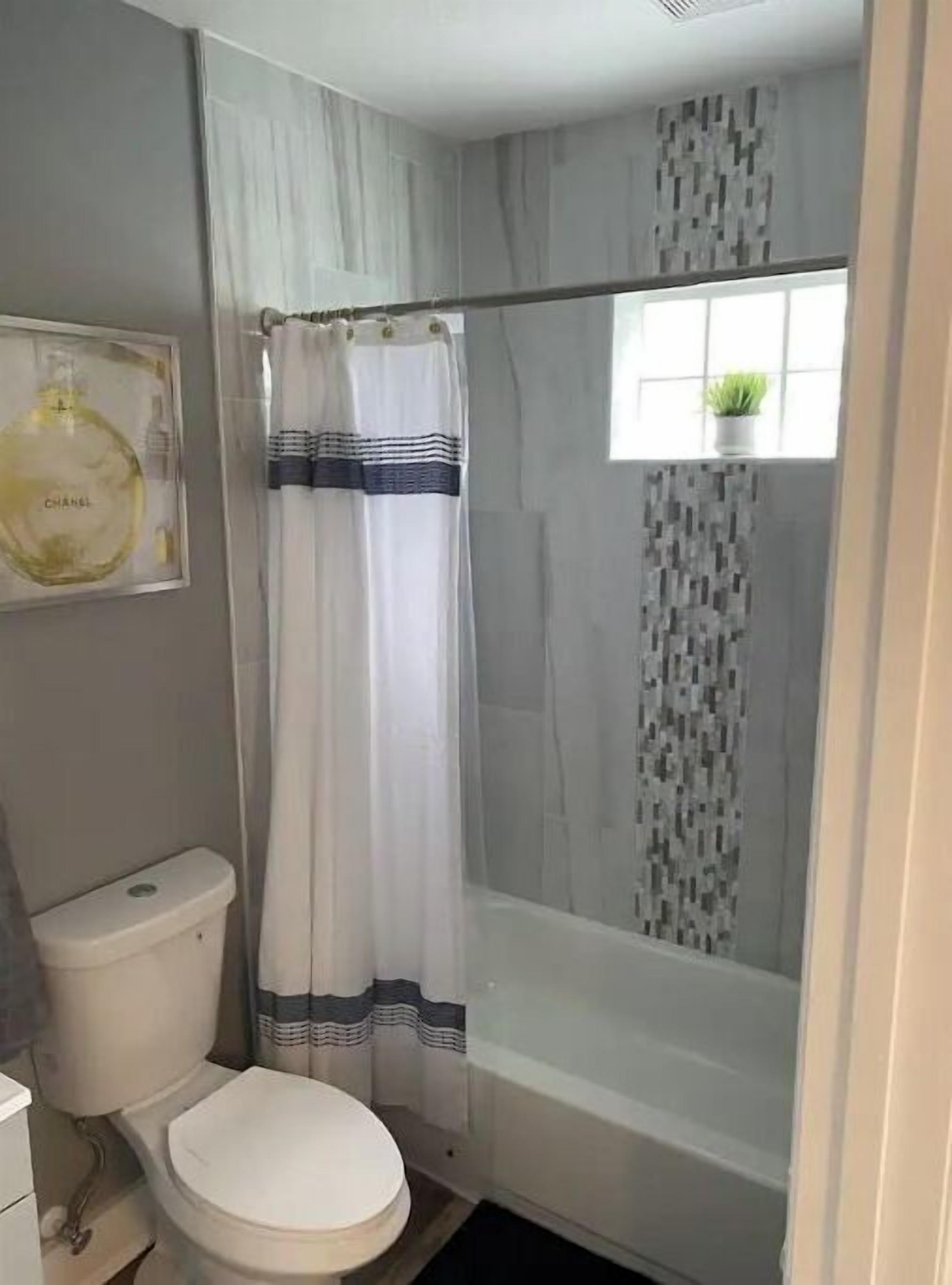 Un baño con inodoro, ducha y una ventana con una planta.