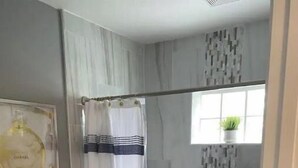 A bathroom with a toilet, shower, and a window with a plant.