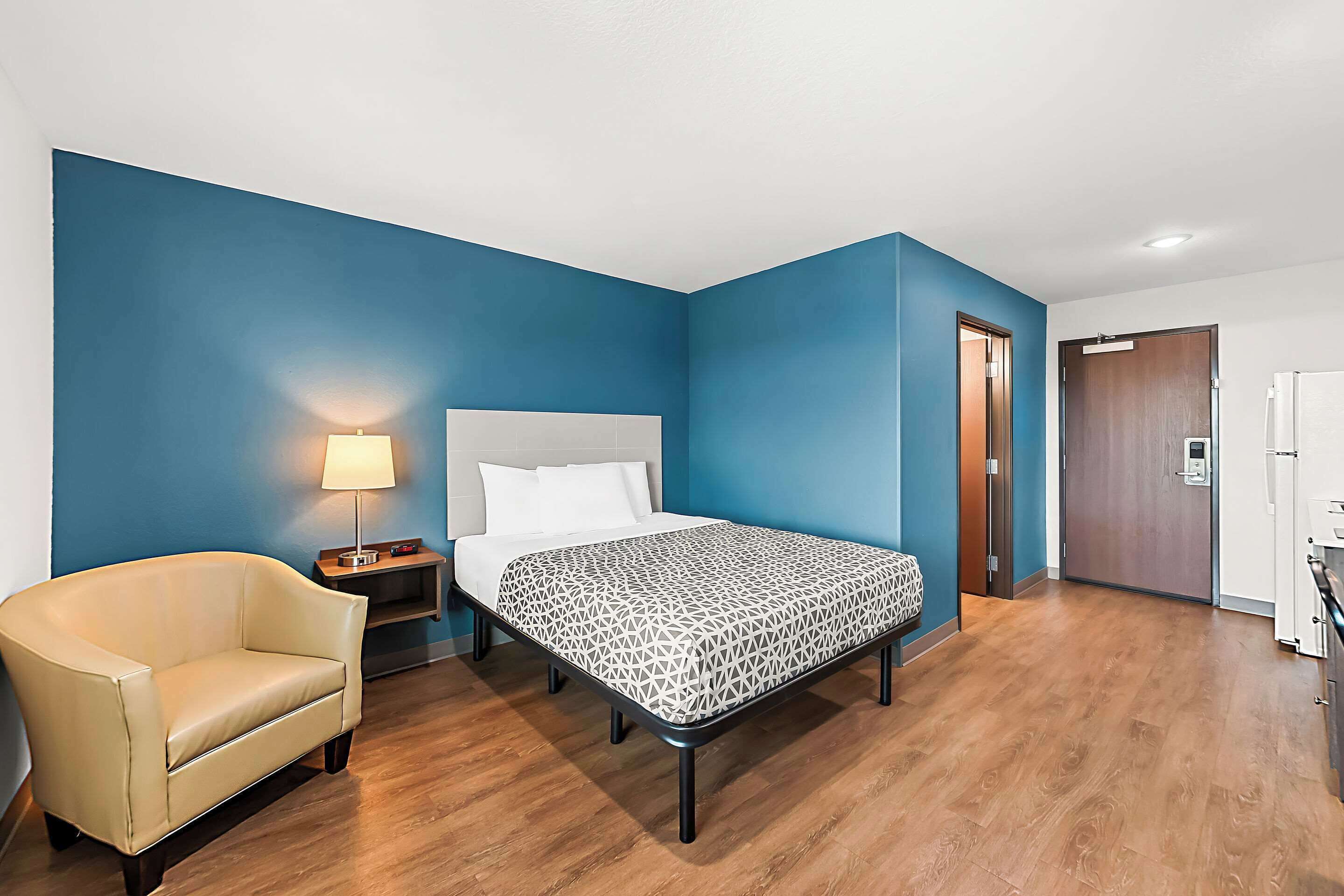 A hotel room with a bed, a chair, a nightstand, and a lamp.