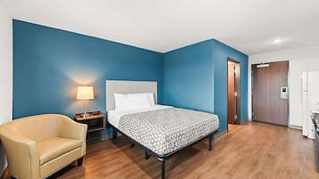 A hotel room with a bed, a chair, a nightstand, and a lamp.
