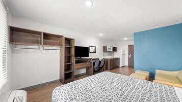 A modern hotel room with a large bed, a desk with a chair, a TV, and a kitchenette.