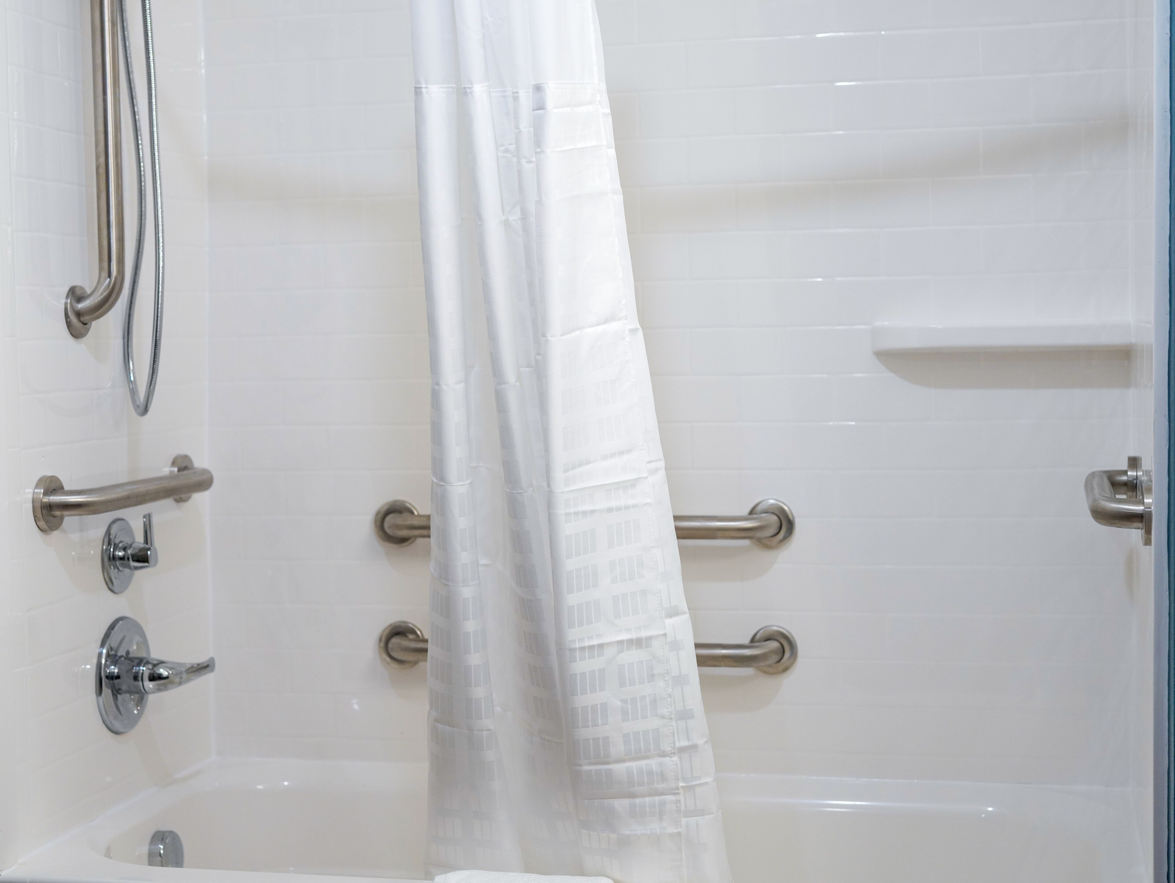 A white bathtub with a showerhead, grab bars, and a curtain.