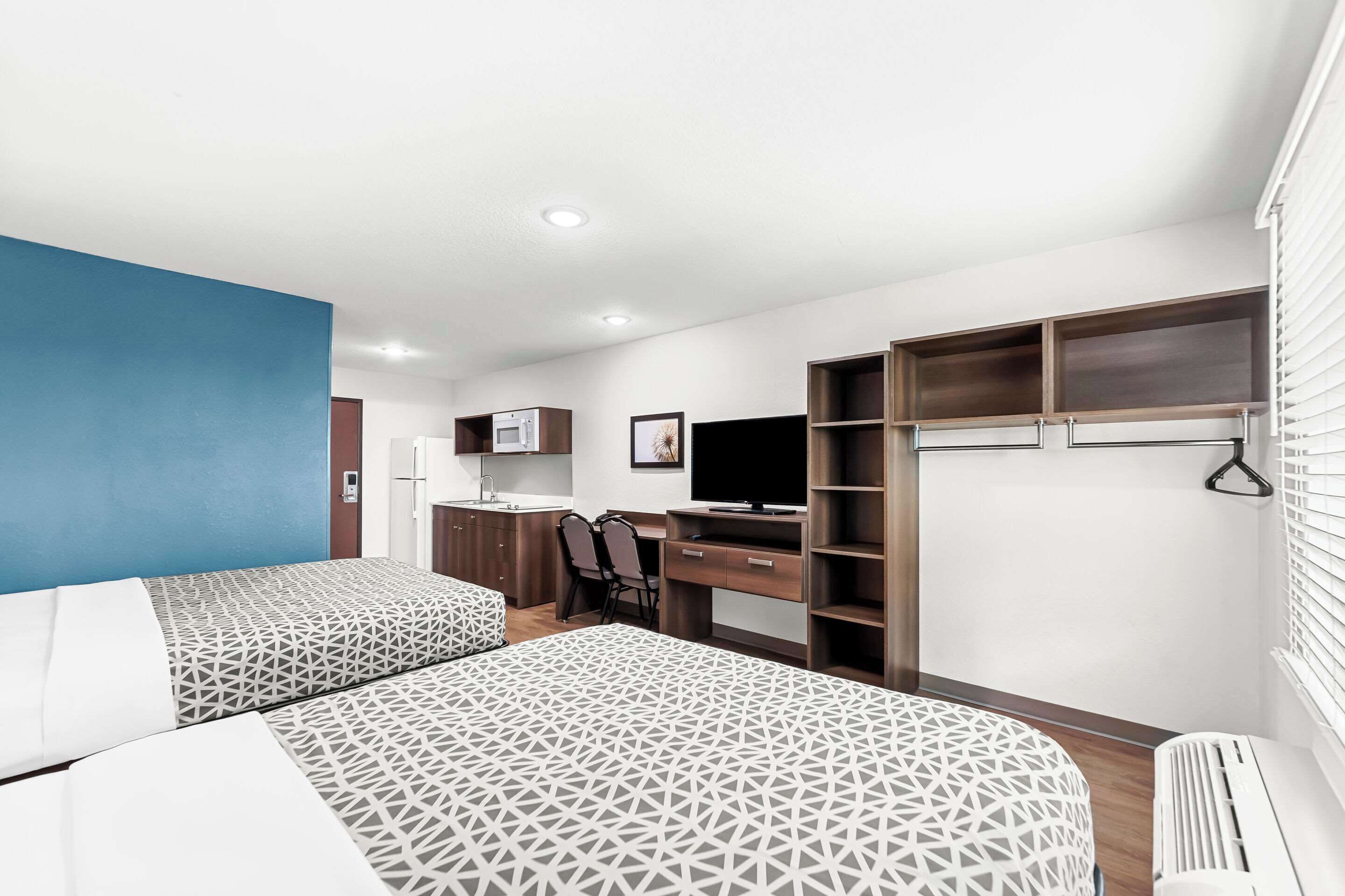 A modern hotel room with two beds, a desk, a TV, and built-in wardrobes.