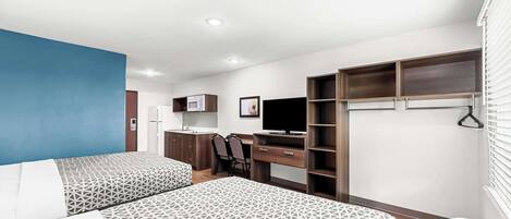 A modern hotel room with two beds, a desk, a TV, and built-in wardrobes.